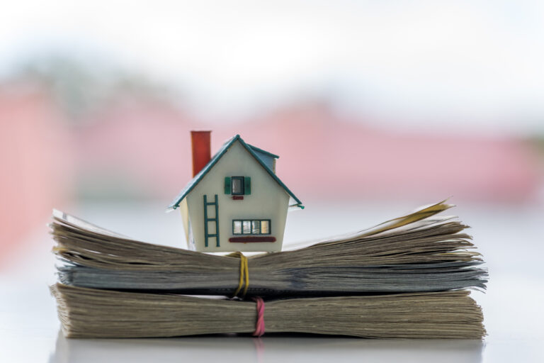 A small model of a house on top of a stack of dollar bills, representing a house purchase
