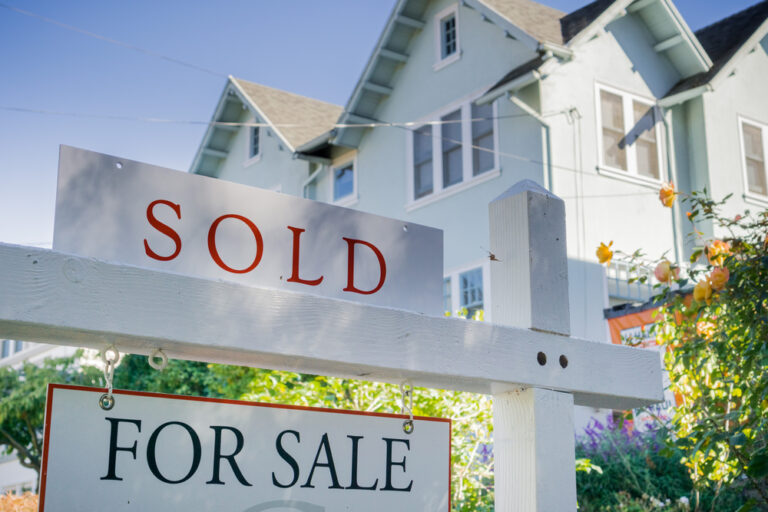 An image of a 'For Sale' Sign with another that says 'Sold' in front of a nice well-lit house.